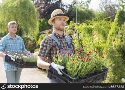 Male gardeners walking while carrying flower pots in crates at plant nursery