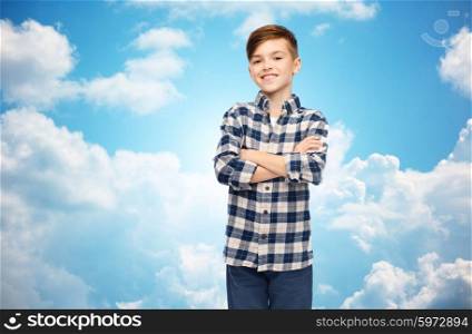 male, gender, childhood, fashion and people concept - smiling boy in checkered shirt and jeans over blue sky and clouds background