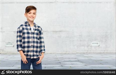 male, gender, childhood, fashion and people concept - smiling boy in checkered shirt and jeans over urban street background