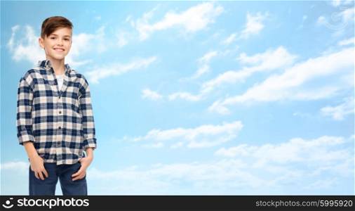 male, gender, childhood, fashion and people concept - smiling boy in checkered shirt and jeans over blue sky and clouds background
