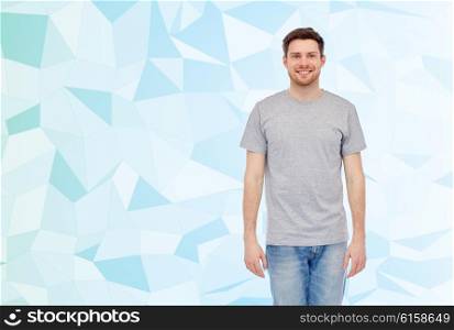 male, gender, fashion and people concept - happy smiling young man in gray t-shirt and jeans over blue low poly texture background,