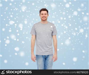 male, gender, fashion and people concept - smiling young man in gray t-shirt and jeans over blue background with snow