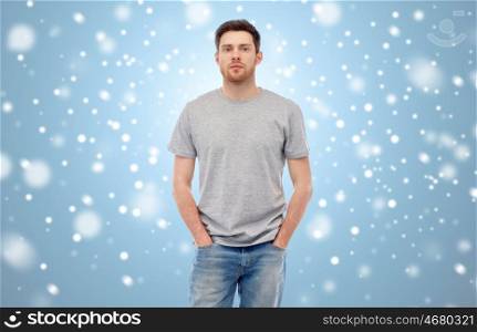 male, gender, fashion and people concept - young man in gray t-shirt and jeans over blue background with snow