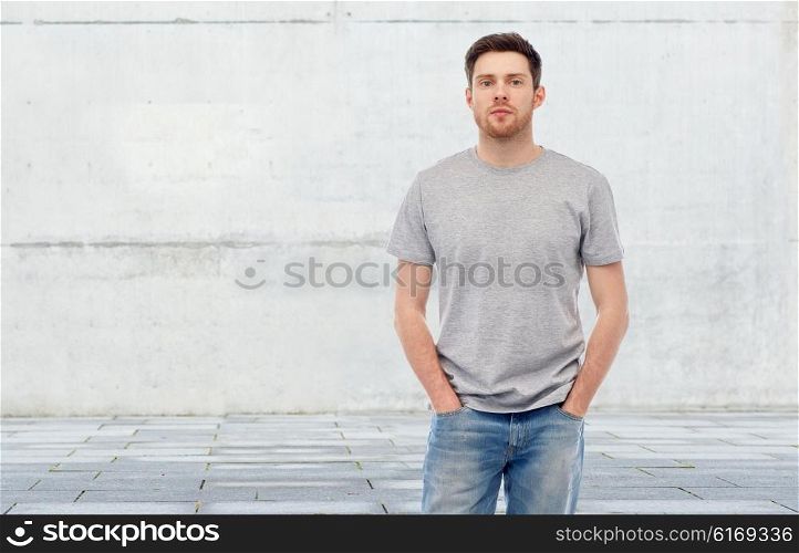 male, gender, fashion and people concept - young man in gray t-shirt and jeans over concrete gray wall on city street background