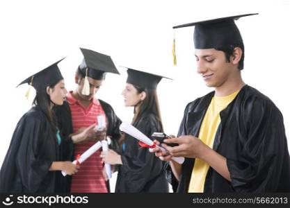 Male graduate student using mobile phone with friends discussing over white background