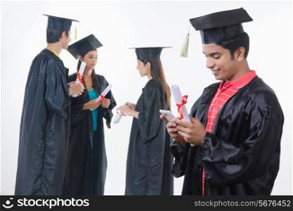 Male graduate student using smart phone with friends discussing against white background