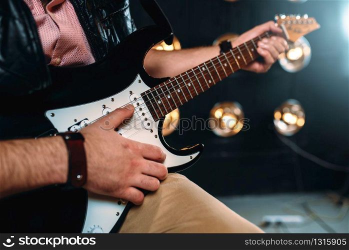 Male guitarist hands performing music on the stage with the decorations of lights. Musical solo concert. Male rock star with electro guitar on the stage