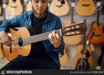 Male guitarist plays on acoustic guitar in music store. Assortment in musical instruments shop, musician buying equipment. Guitarist plays on acoustic guitar in music store