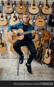 Male guitarist plays on acoustic guitar in music store. Assortment in musical instruments shop, musician buying equipment