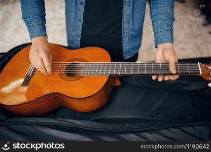 Male guitarist puts acoustic guitar in the case in music store. Assortment in musical instruments shop. Guitarist puts guitar in the case, music store