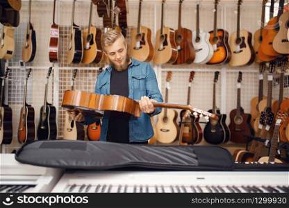Male guitarist puts acoustic guitar in the case in music store. Assortment in musical instruments shop, musician buying equipment. Guitarist puts guitar in the case, music store