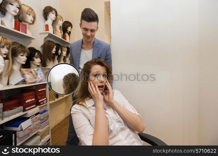 Male hairstylist showing hair to worried female customer in salon