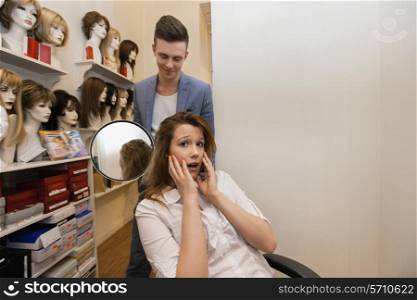 Male hairstylist showing hair to worried female customer in salon