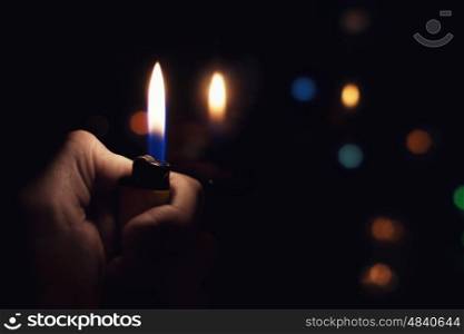 Male hand holding a burning lighter in the dark