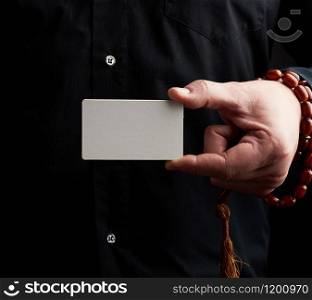 male hand holding a rectangular blank white paper business card, man wearing a black shirt, place for inscription