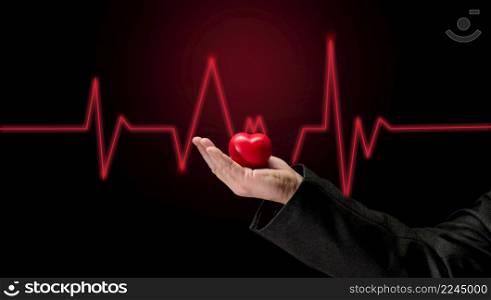 Male hand holding a red heart on a dark background, early diagnosis of the cardiovascular system
