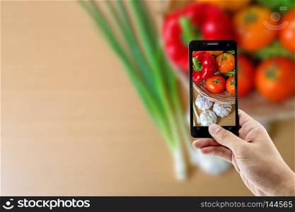 male hand holding a smartphone against of fresh produce at basket