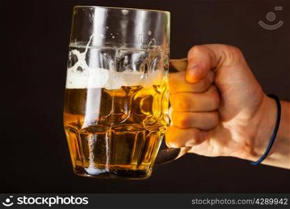 Male hand holding mug of beer dark background