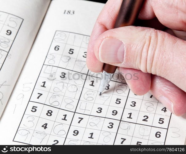 Male hand holding pen or pencil on suduko puzzle