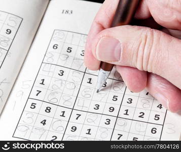 Male hand holding pen or pencil on suduko puzzle