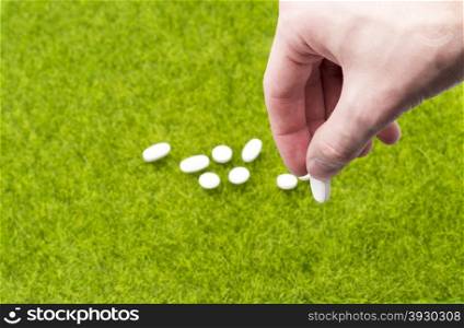 Male hand holding pill on background of tablets spilling on the grass. Male hand holding tablet on background of pills spilling on the green grass