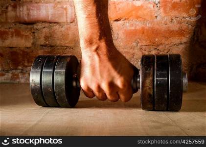 male hand is holding metal barbell against brick wall