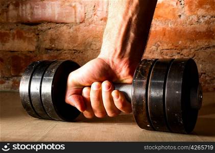 male hand is holding metal barbell against brick wall