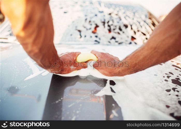 Male hand rubbing the car with foam, automobile in suds. Carwash station. Male hand rubbing the car with foam, carwash