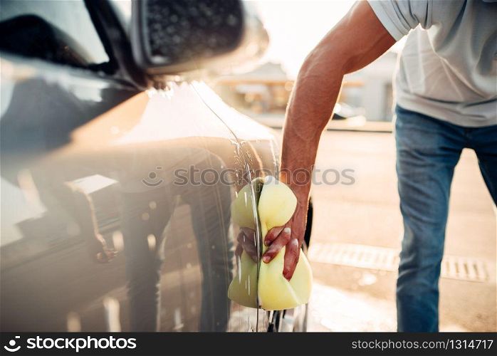 Male hand rubbing the car with foam, automobile in suds. Carwash station. Male hand rubbing the car with foam, carwash