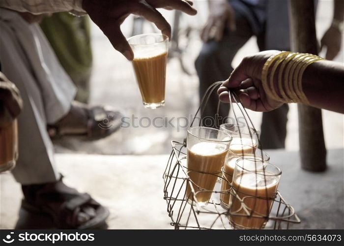 Male hand taking a glass of chai from tray held by woman