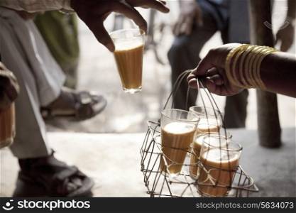 Male hand taking a glass of chai from tray held by woman