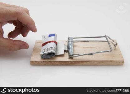 Male hand taking rolled up euro bills from mousetrap