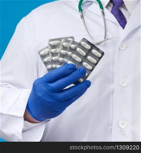 male hand with blue sterile gloves holds a stack of pills in a blister, concept for drug treatment of diseases, blue background