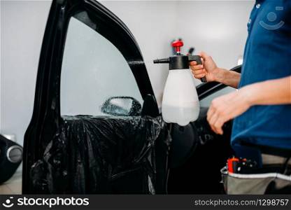 Male hand with spray, car window tint installation process, installing procedure, tinting film. Male hand with spray, car window tint installation