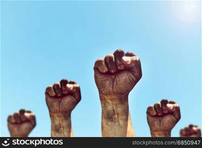 Male hands are clenched into a fist and raised up against the sky with a bright sun