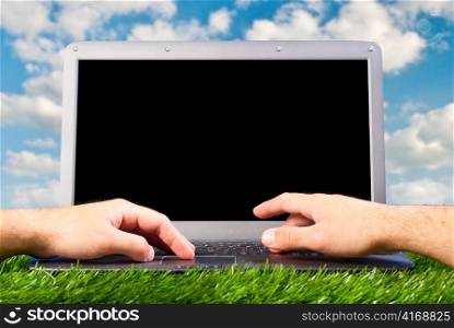 male hands are working on laptop on grass outdoors