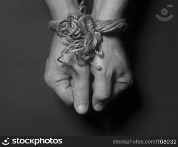 Male hands bound with rope on black