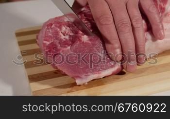 Male hands cutting raw pork meat on wooden cutting board