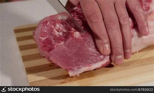 Male hands cutting raw pork meat on wooden cutting board