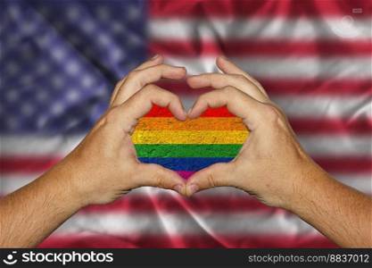 male hands forming a heart with an LGBT flag inside against the background of the USA flag. male hands forming a heart with an LGBT flag