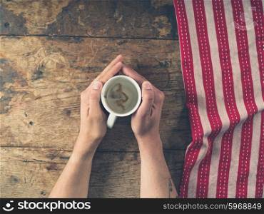 Male hands holding an empty cup on a wooden table with a tea towel