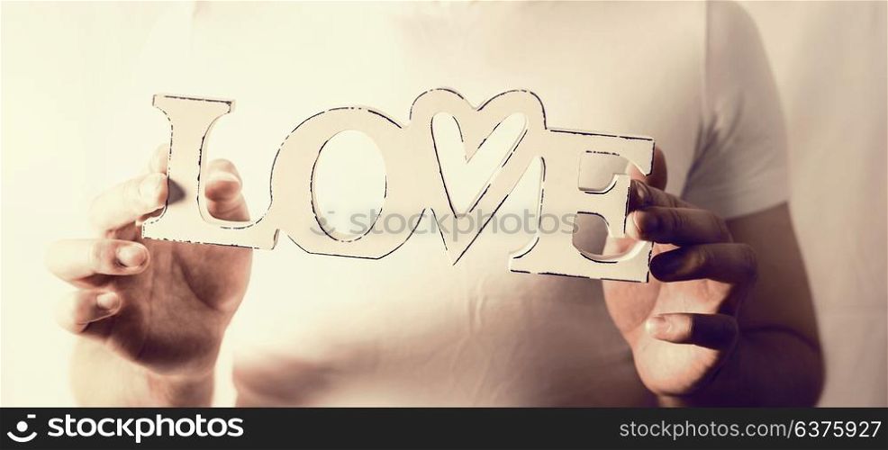Male hands holding word Love at wall background, close up