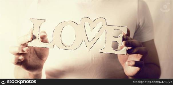 Male hands holding word Love at wall background, close up