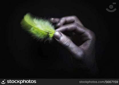 male hands in silver paint holding light green feather