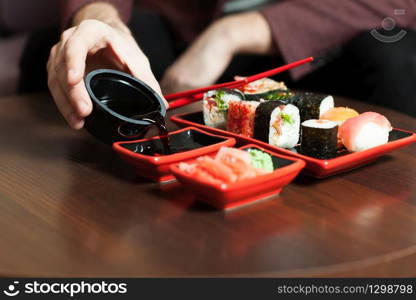 Male hands pours sauce in a plate. Sushi set on wooden table.