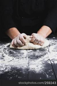 male hands substitute white wheat flour dough on a black wooden background