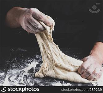 male hands substitute white wheat flour dough on a black wooden background, vintage toning