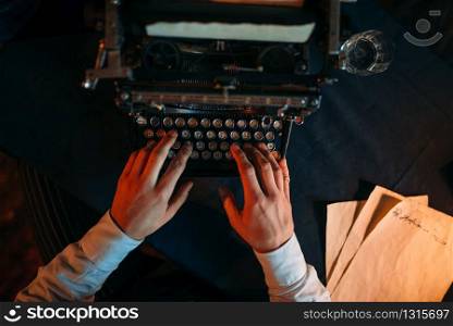Male hands typing on retro typewriter, top view. Dark blue table cloth on background. Writer, journalist, literature author, blogger or poet concept. Male hands typing on retro typewriter