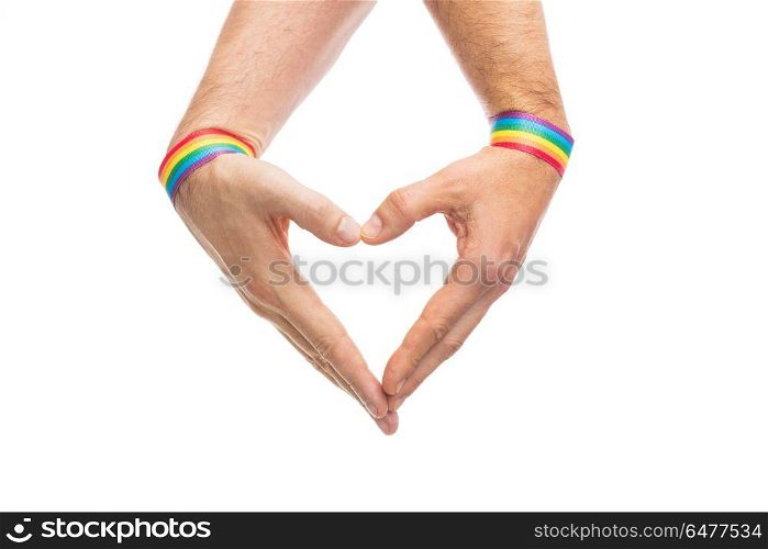 male hands with gay pride wristbands showing heart. lgbt, same-sex love and homosexual relationships concept - close up of male couple hands with gay pride rainbow awareness wristbands showing heart gesture