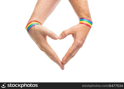 male hands with gay pride wristbands showing heart. lgbt, same-sex love and homosexual relationships concept - close up of male couple hands with gay pride rainbow awareness wristbands showing heart gesture